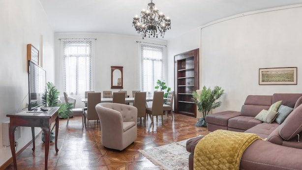Un salon spacieux avec un canapé en cuir marron, un coin repas agrémenté d’un lustre et une bibliothèque.