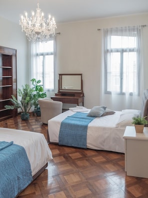 Une chambre d’hôtel avec deux lits, un plancher en bois, un lustre, un miroir et une plante.