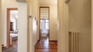 Un couloir au plancher de bois mène à une chambre à coucher équipée d’un lit et à une salle de bain avec des toilettes.
