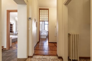 A hallway with a wooden floor leading to a bedroom with a bed and a bathroom with a toilet.