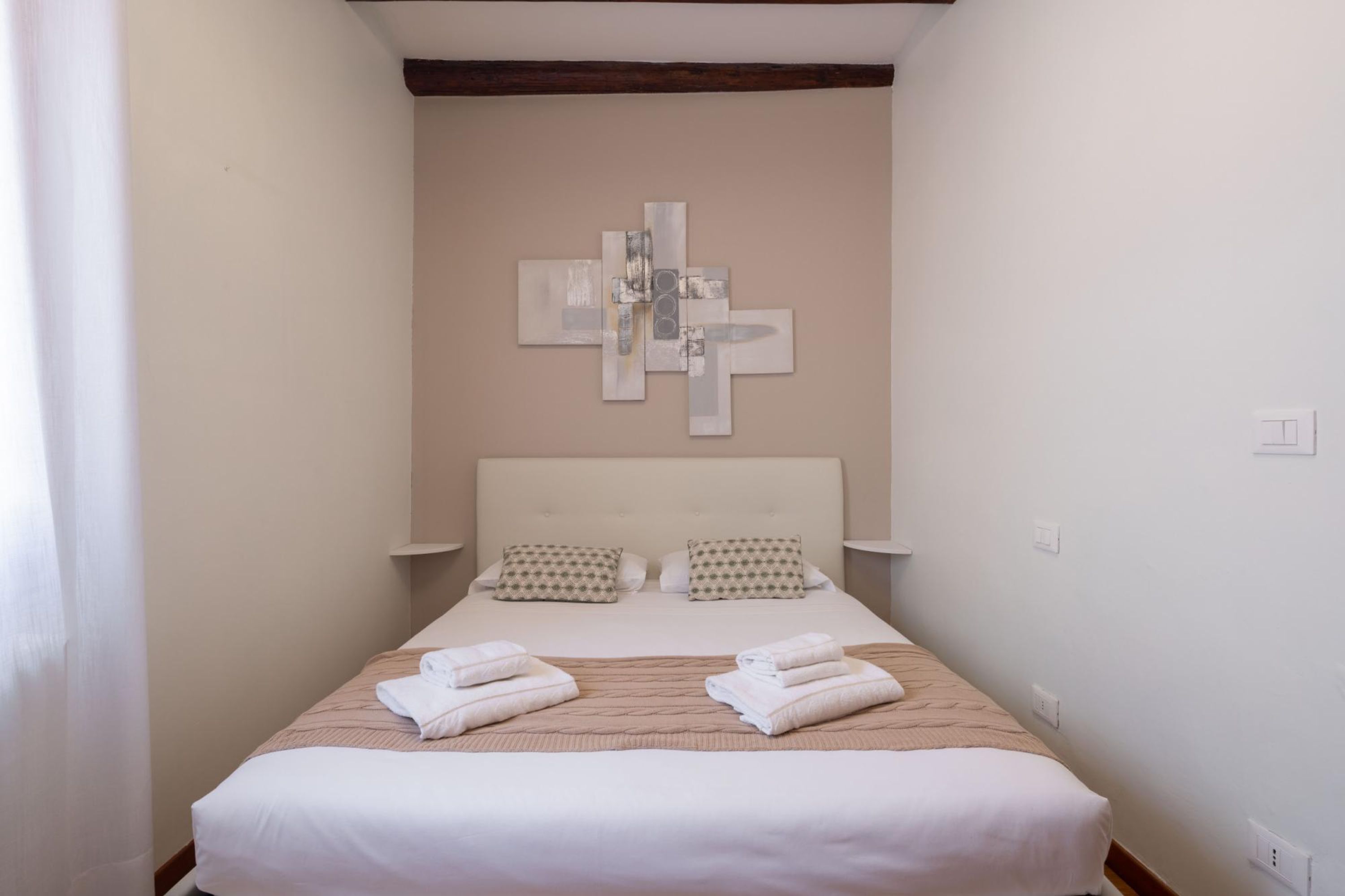 Un lit bien fait, agrémenté d’oreillers et de serviettes pliées, une œuvre d’art abstraite moderne accrochée au mur au-dessus, et une décoration simple et épurée.