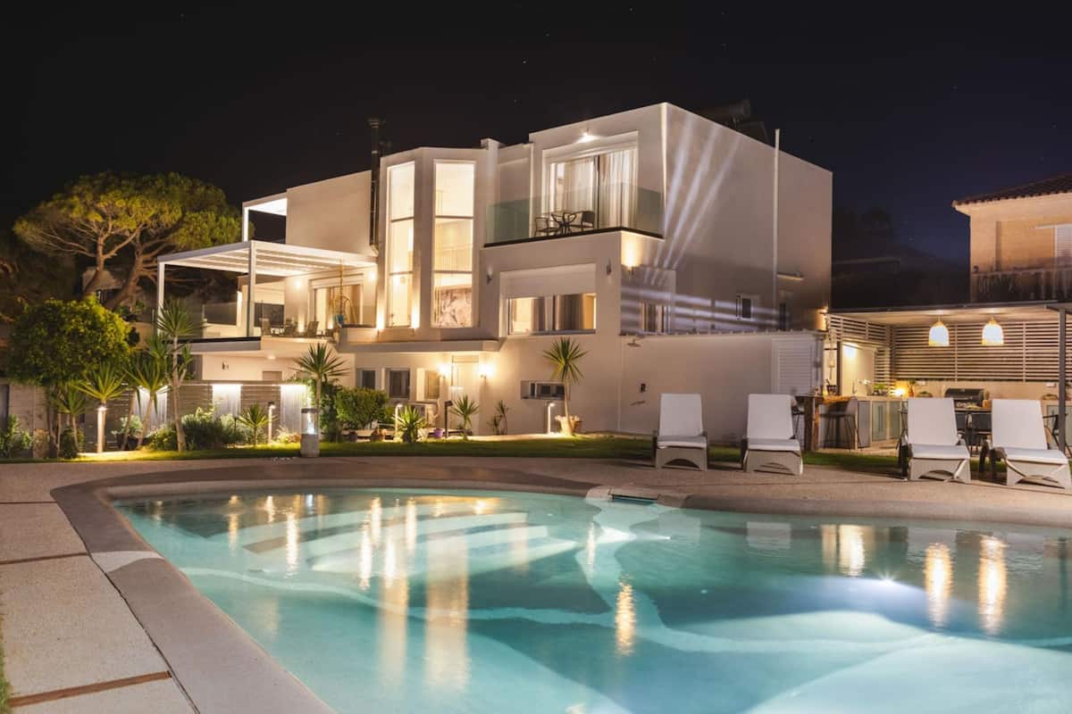 Una casa moderna de dos pisos con piscina, mobiliario exterior y ventanas bien iluminadas.