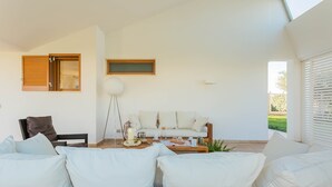 A modern living room with a sofa, coffee table, and a small table with drinks. There is a window with blinds and a view of greenery outside. - Affittacamere Incanto nel Verde by Wonderful Italy (Polignano a Mare)