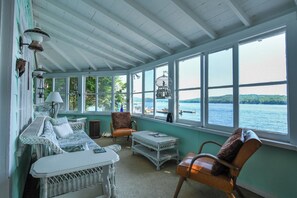 A cozy room with wicker furniture, large windows, and a view of the water. - Charming cottage just 12' from the water's edge with gorgeous sunrise views! (Bridgton)