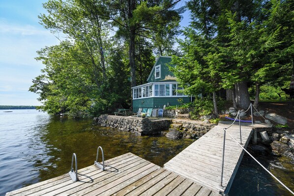 A wooden dock leading to a house by a lake, surrounded by trees.