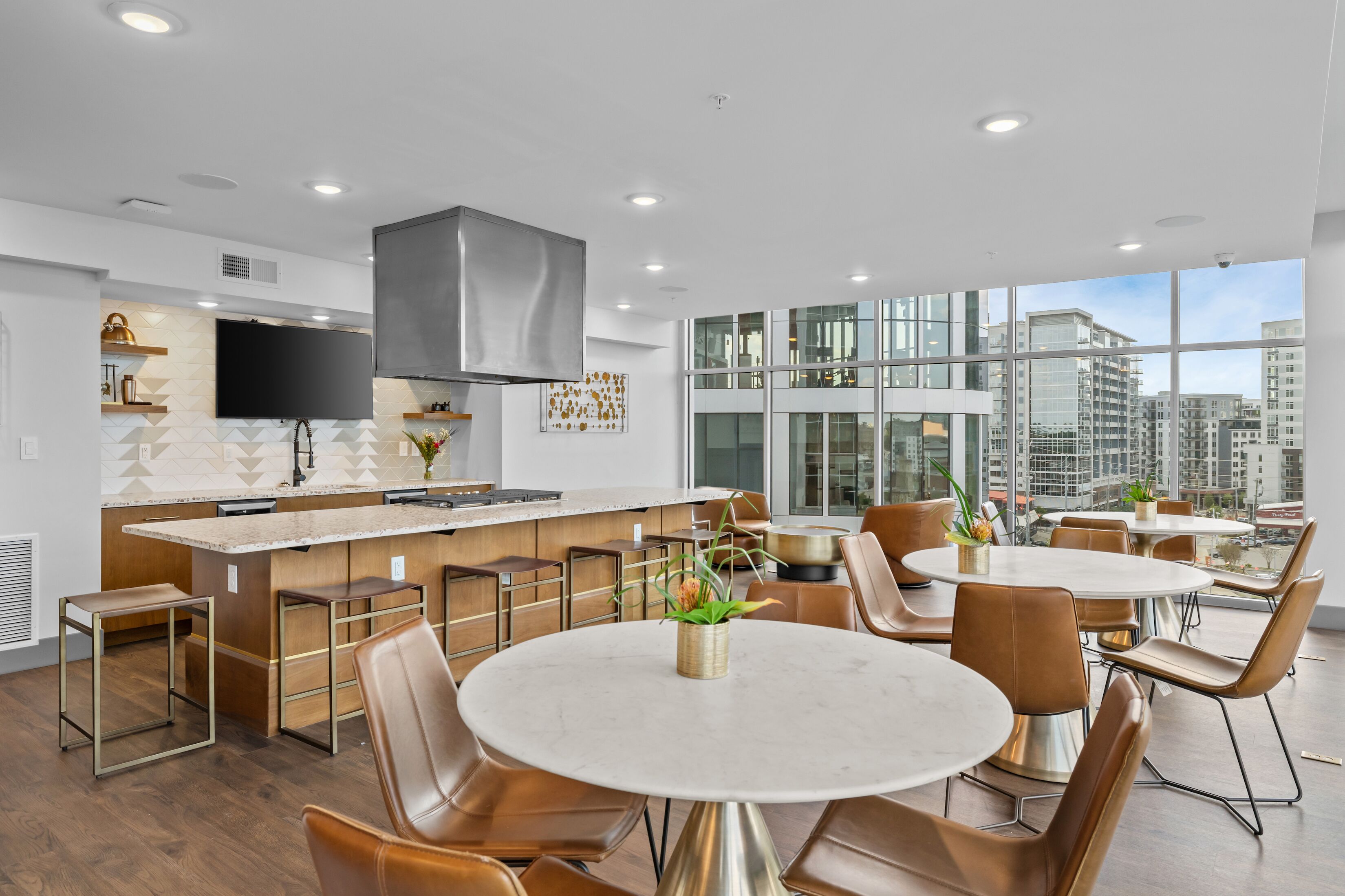 A modern kitchen with a large island, bar seating, and a dining area with round tables and chairs.