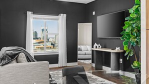 A modern living room with a large window, a flat-screen TV, a ceiling fan, and a plant. - Midnight Manor Penthouse Suite The Gulch (Nashville)