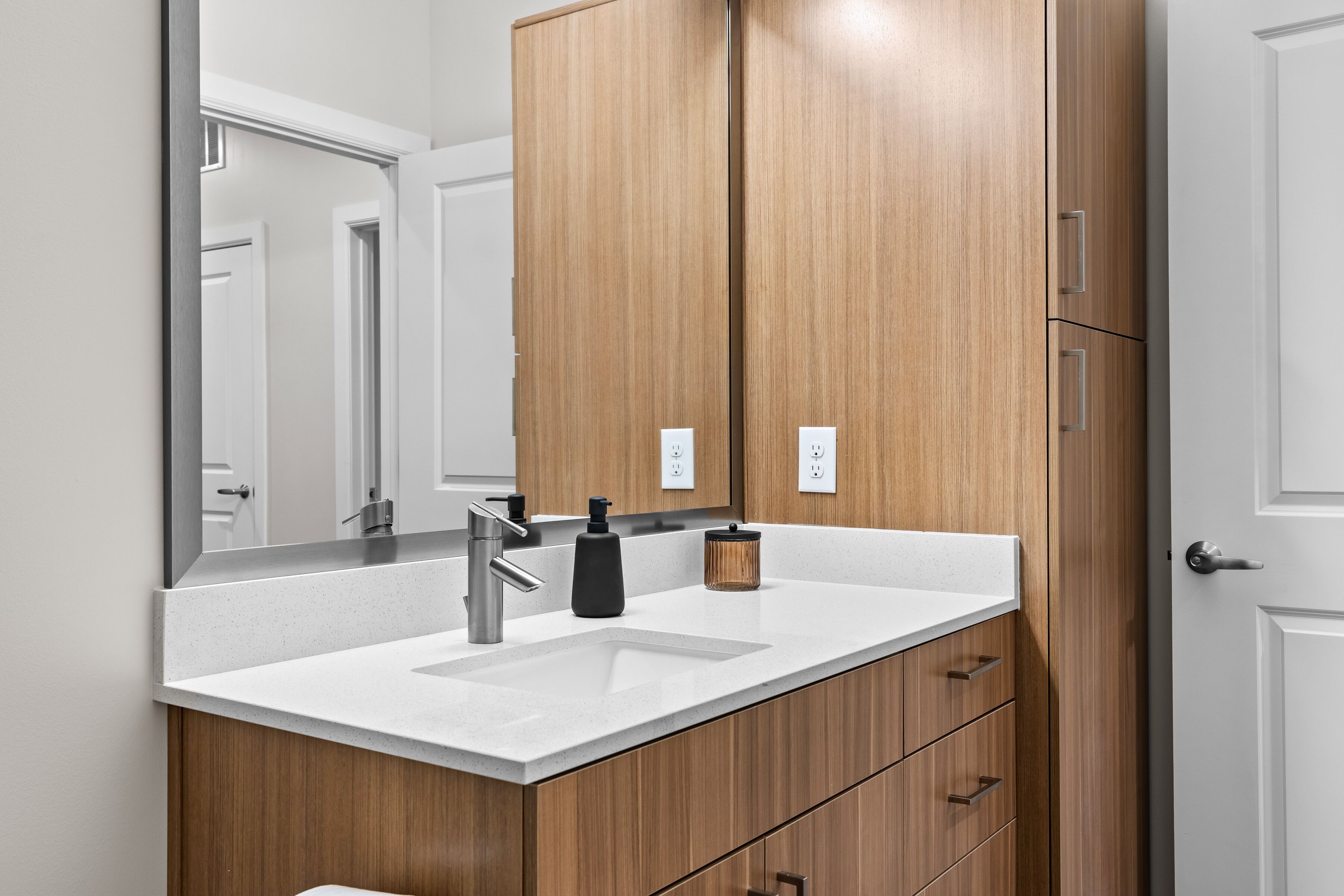 A modern bathroom with a wooden vanity, a white sink, and a large mirror.