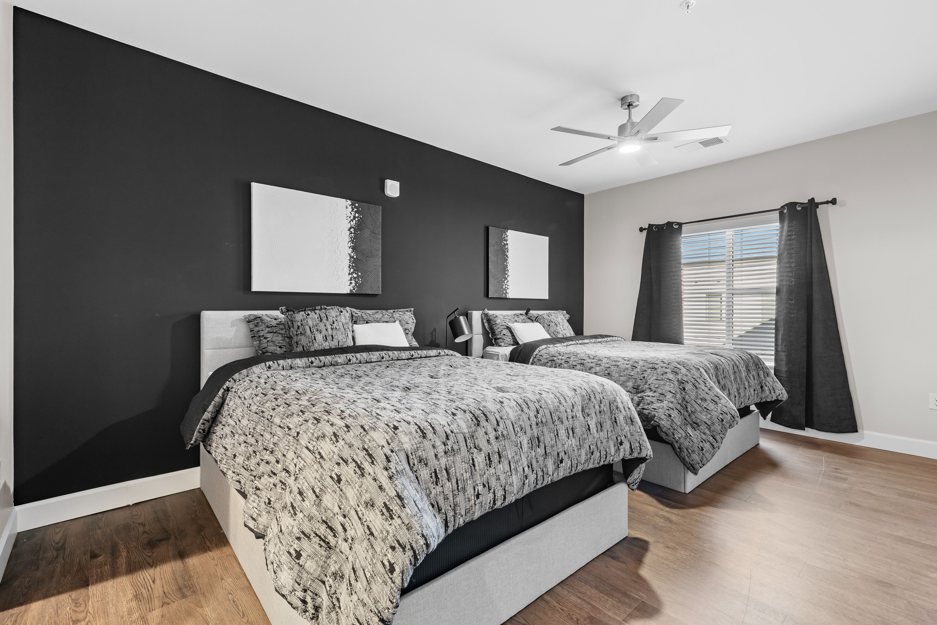 A modern bedroom with two beds, a ceiling fan, and a window with curtains.