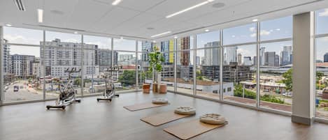 A spacious gym with large windows, exercise equipment, and a city view.