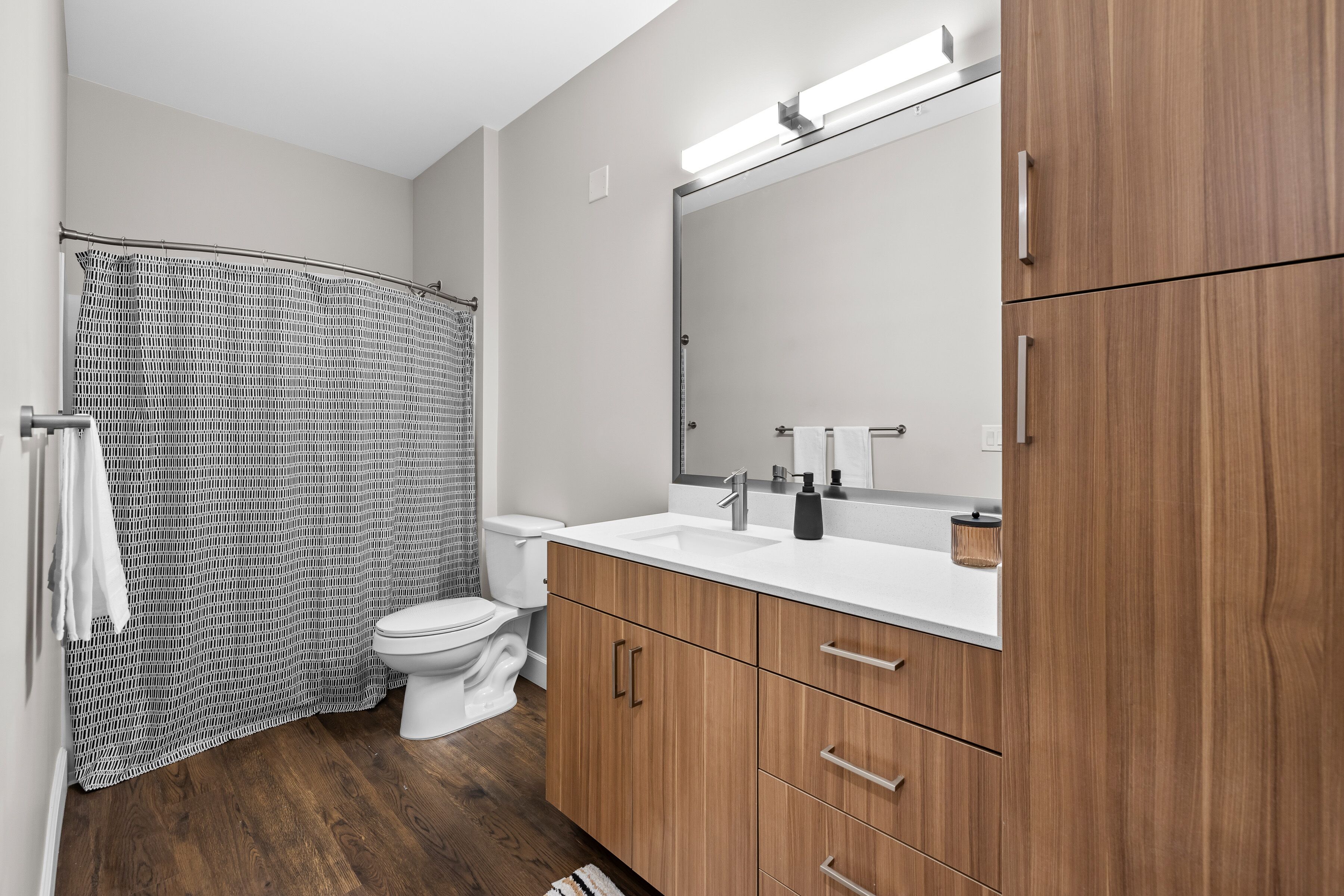 Un baño moderno con cortina de ducha, inodoro, tocador con espejo y armarios de madera.