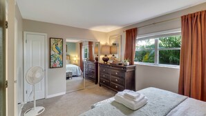 Une chambre à coucher avec un grand lit, une commode, un miroir, un ventilateur et une fenêtre avec des rideaux.