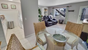 Un salon moderne avec une table à manger en verre, des chaises en osier, un canapé en cuir et un escalier menant à l’étage supérieur.