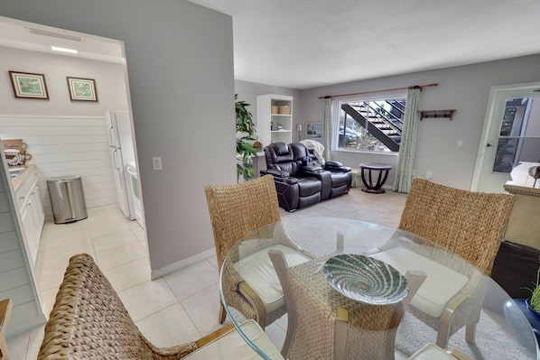 A modern living room with a glass dining table, wicker chairs, a leather sofa, and a staircase leading to an upper floor.