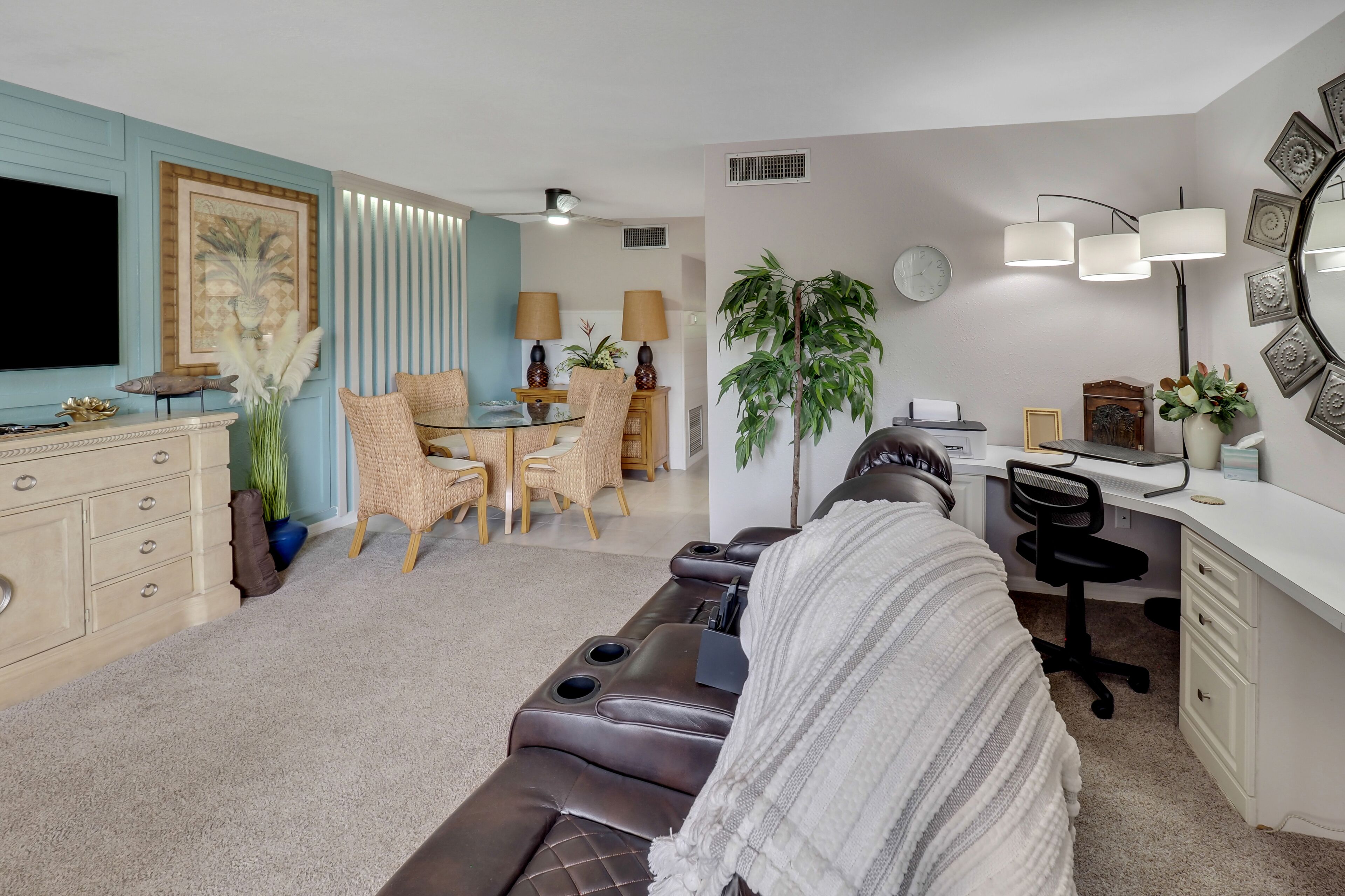 A modern living room with a sofa, a dining area with chairs, a TV, and a desk with a chair.