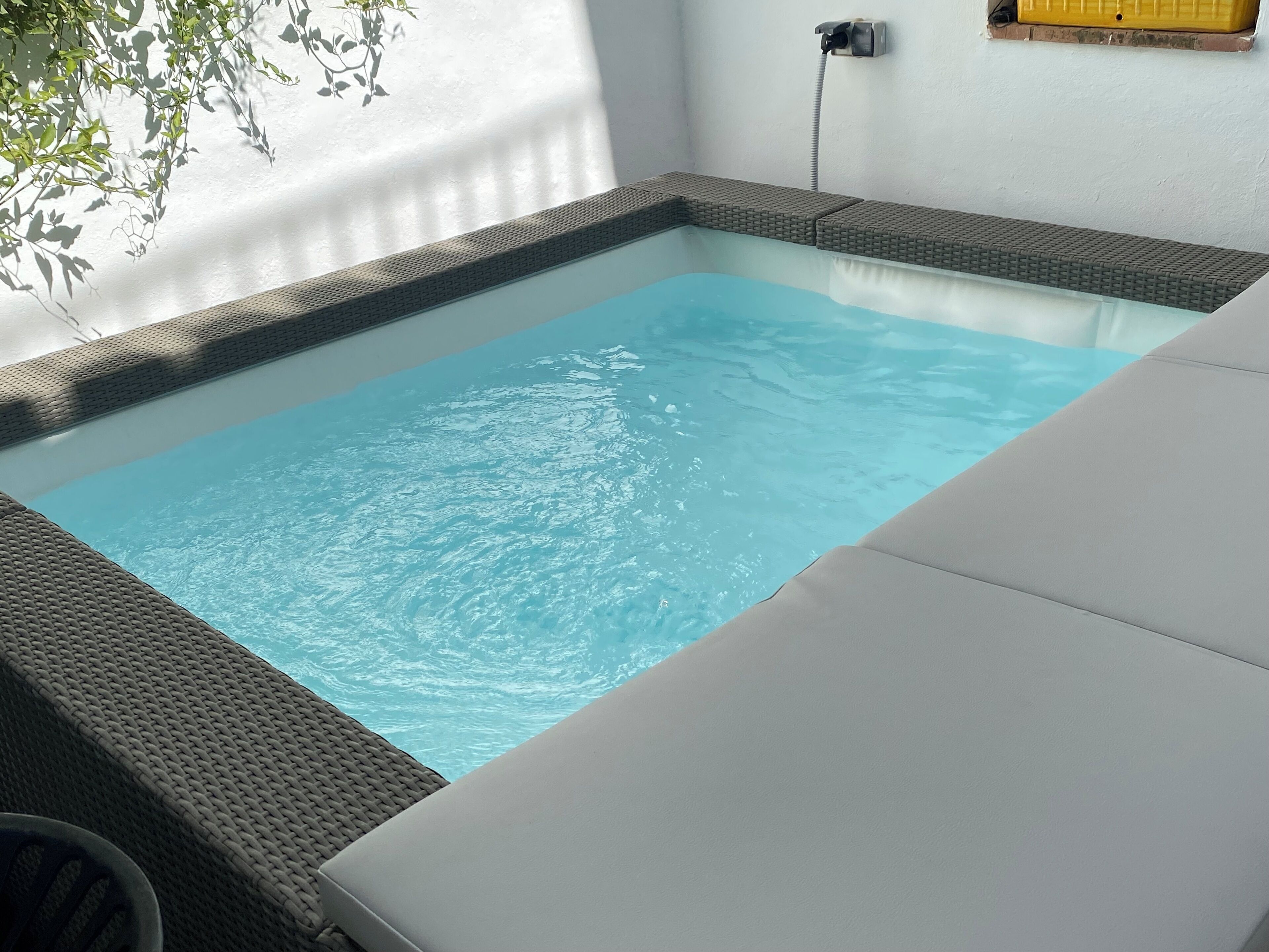 Una piscina rectangular con borde texturizado, rodeada por una zona de descanso blanca y un teléfono instalado en la pared.