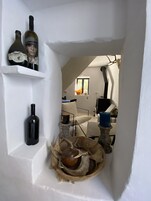 Un pasillo estrecho con paredes blancas, un cofre de madera y dos botellas de vino en un estante.