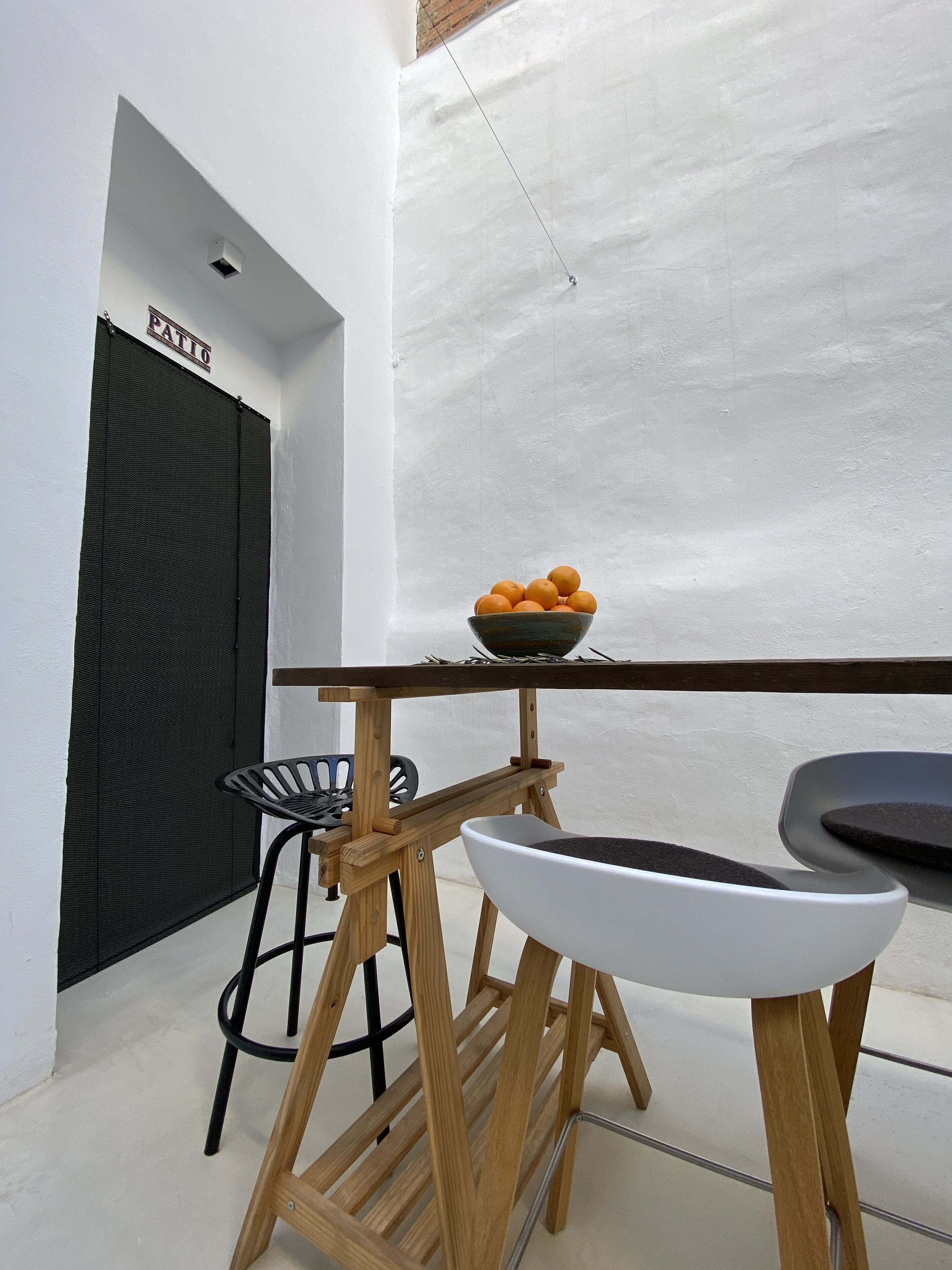A compact kitchen with a wooden table, a bowl of oranges, and a black chair.