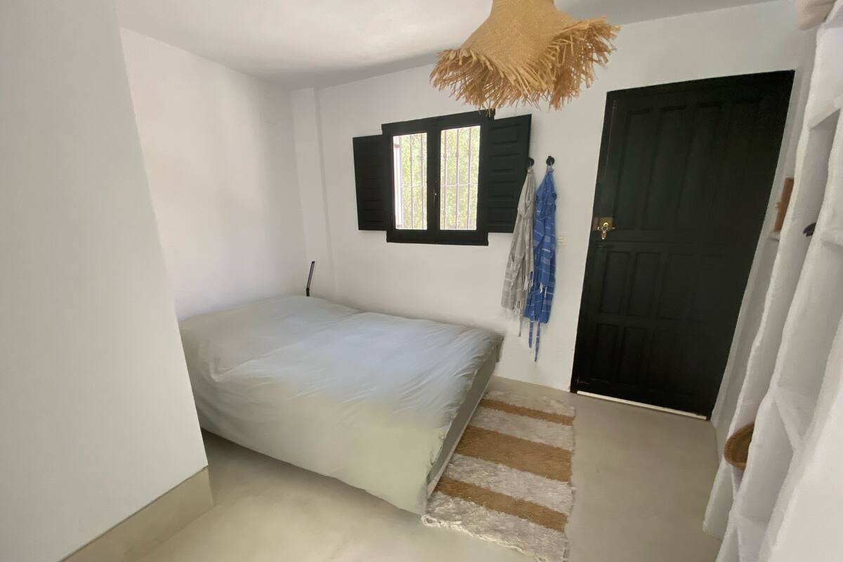 A bedroom with a bed, a window with shutters, a door, and a striped rug.