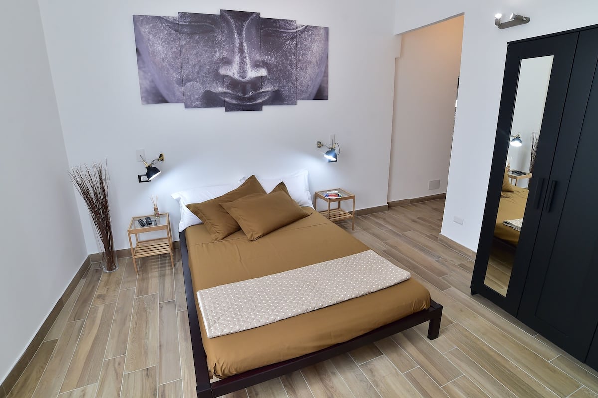 A bedroom with a bed, bedside tables, wall art, and a mirror.