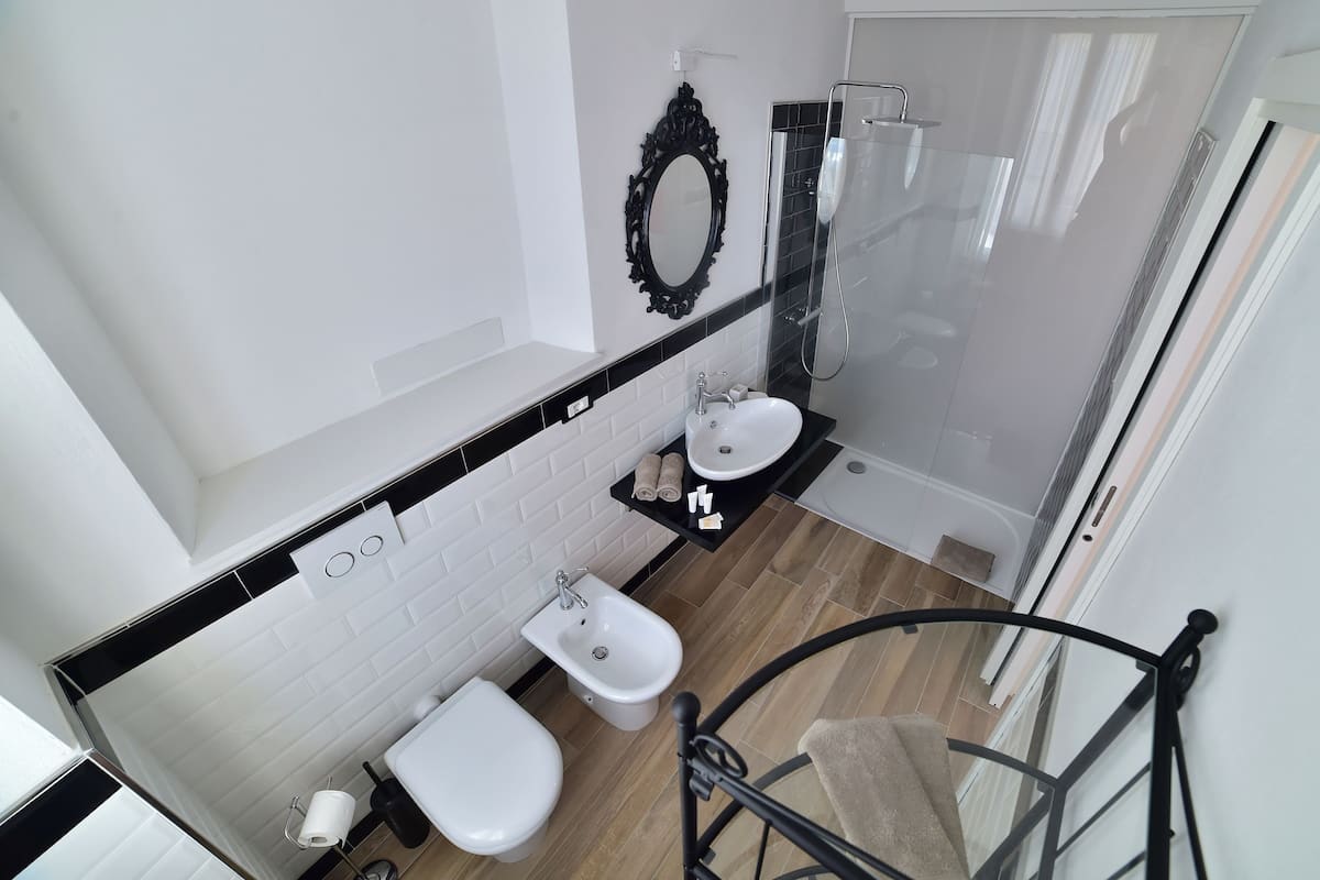 A modern bathroom with a white sink, toilet, and bidet, a glass shower enclosure, and a black-framed mirror.