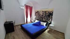 Un dormitori amb llit, una tauleta de nit, aire condicionat fixat a la paret, cortina vermella i un mural amb vista a la ciutat.