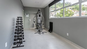 A gym with exercise equipment, a dumbbell rack, and a window with a view of buildings. - New studio near Beiramar Shopping #HKS18D (Florianópolis)