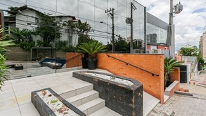 A modern building with a glass facade, outdoor seating area, and a brick wall with steps leading to a rooftop garden. - New studio near Beiramar Shopping #HKS18D (Florianópolis)