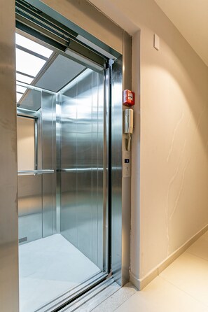 An elevator with metallic walls, a control panel, and a red emergency button.