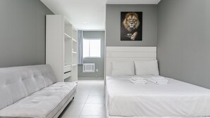A modern bedroom with a white bed, a white sofa, a grey wall, and a lion painting. - New studio near Beiramar Shopping #HKS18D (Florianópolis)