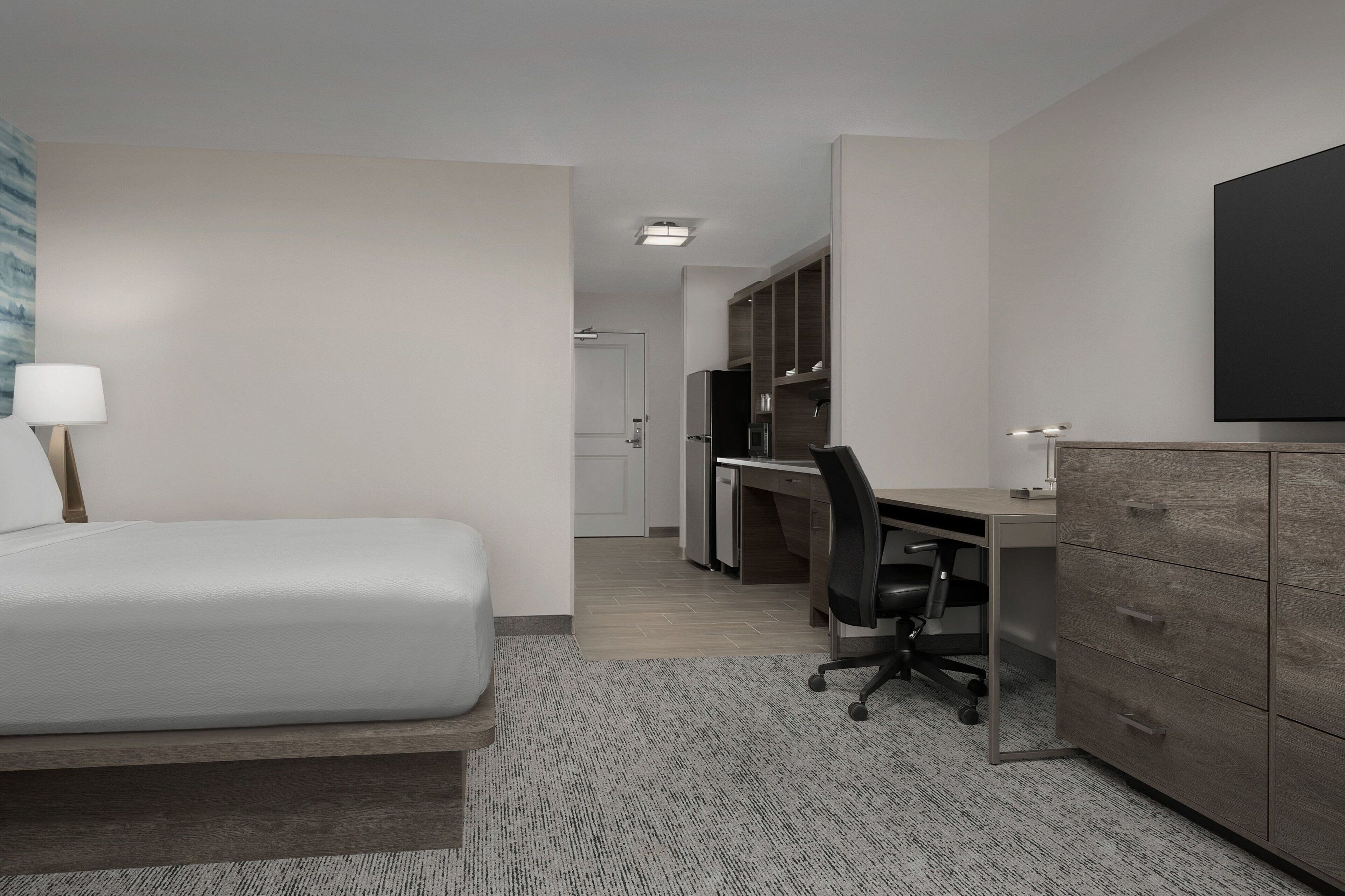 Ett modernt hotellrum med en säng, ett skrivbord och en garderob.