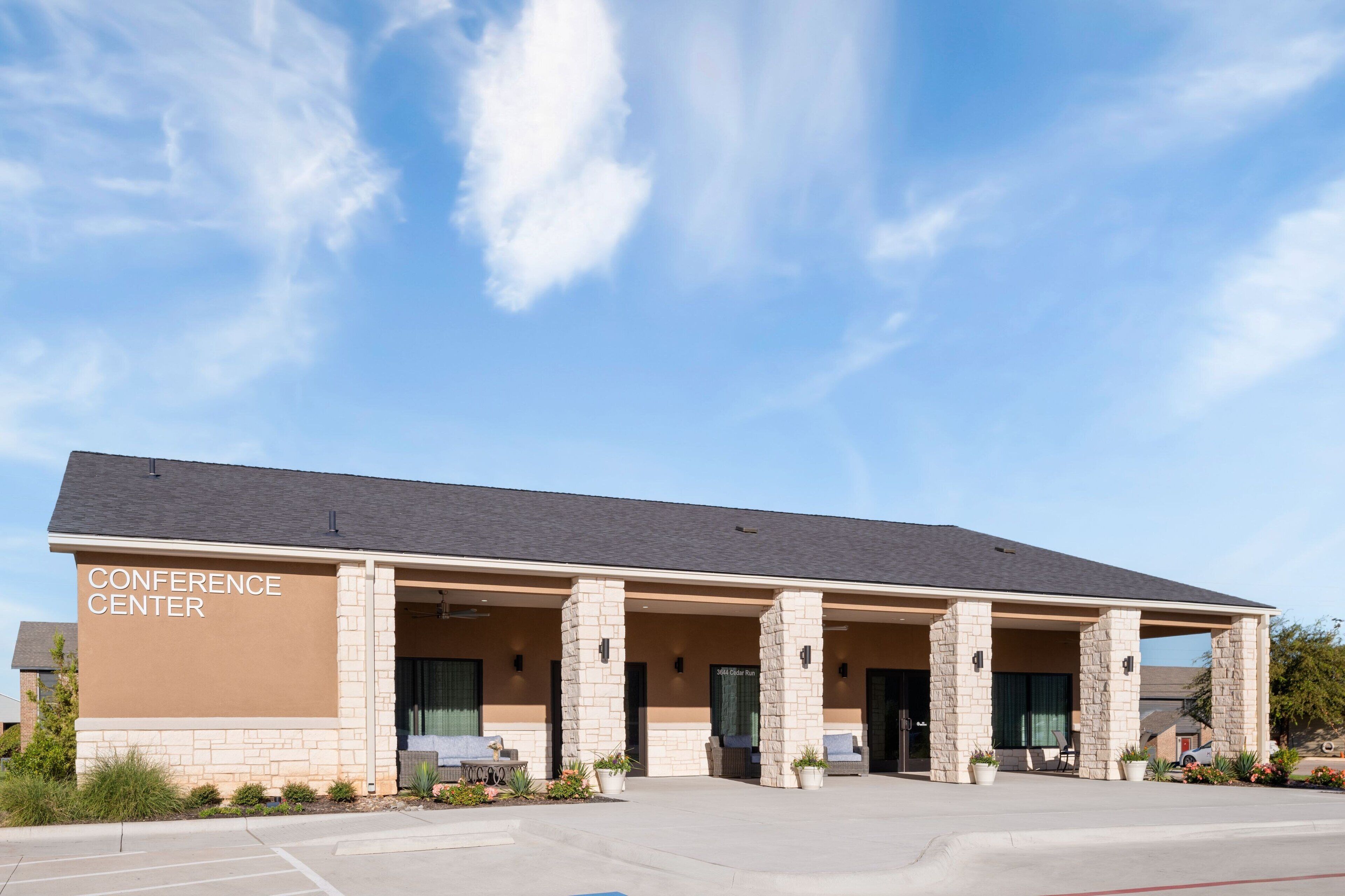 A building labeled "CONFERENCE CENTER" with a covered entrance, outdoor seating, and a parking lot.