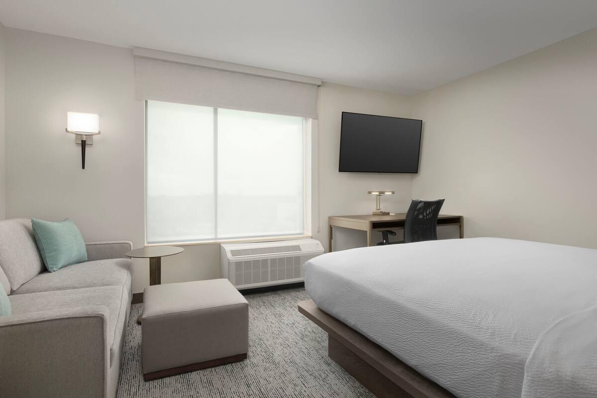 A hotel room with a bed, a desk, a chair, a sofa, and a flat-screen TV.