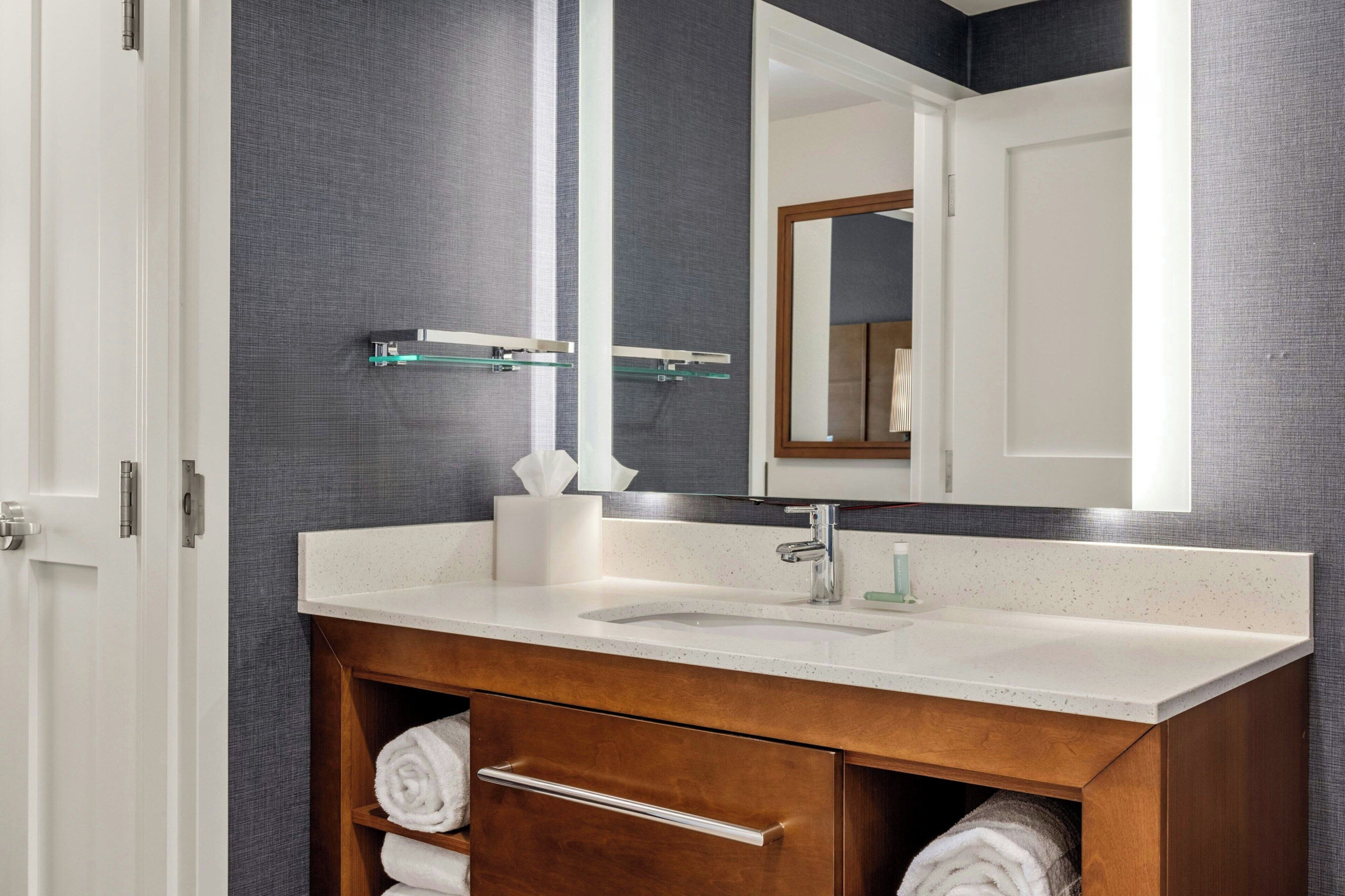 Un baño con lavamanos blanco, tocador de madera y un espejo grande.