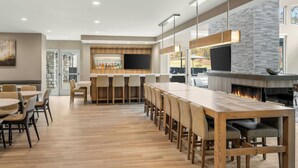 A modern bar area with a long wooden table, bar stools, and a stone accent wall. - Residence Inn by Marriott Homewood Mountain Brook (Birmingham)