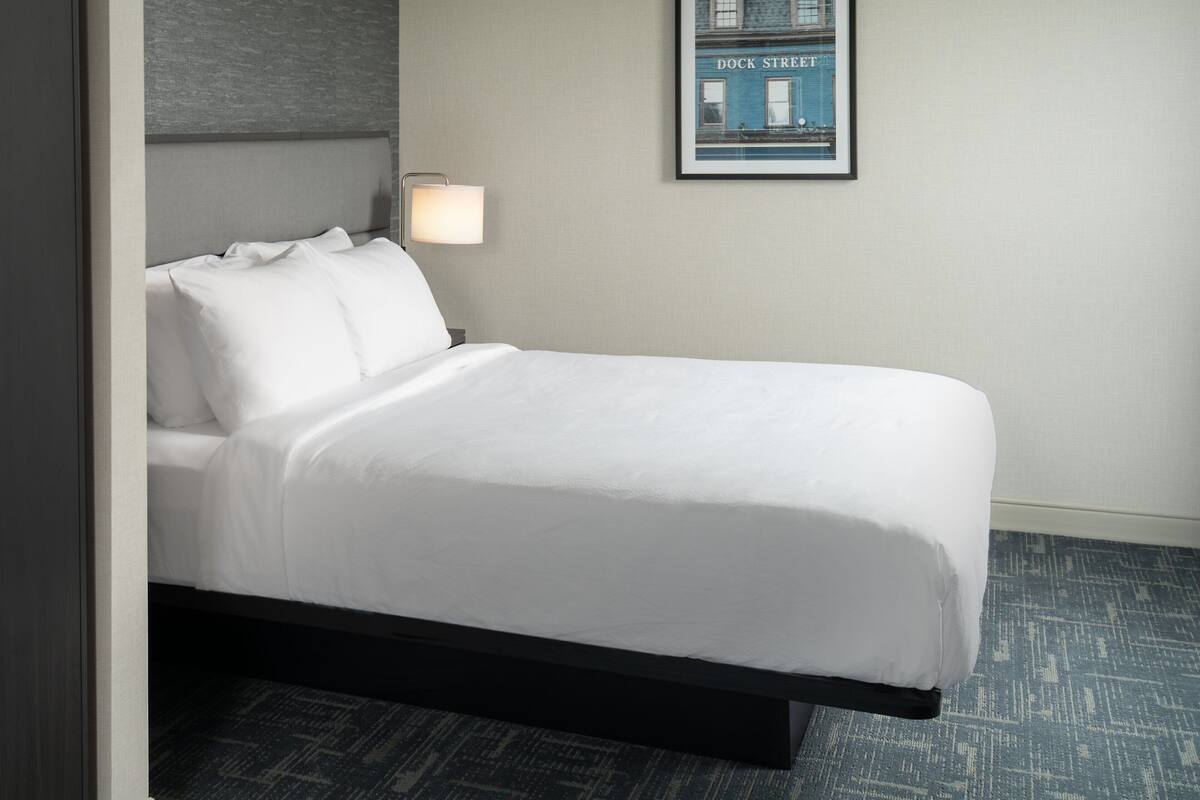 Un lit bien fait, avec des draps blancs, une tête de lit et un tableau encadré accroché au mur.