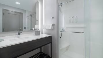 Uma casa de banho moderna com cabine de duche em vidro, um espelho grande e toucador com bancada escura.