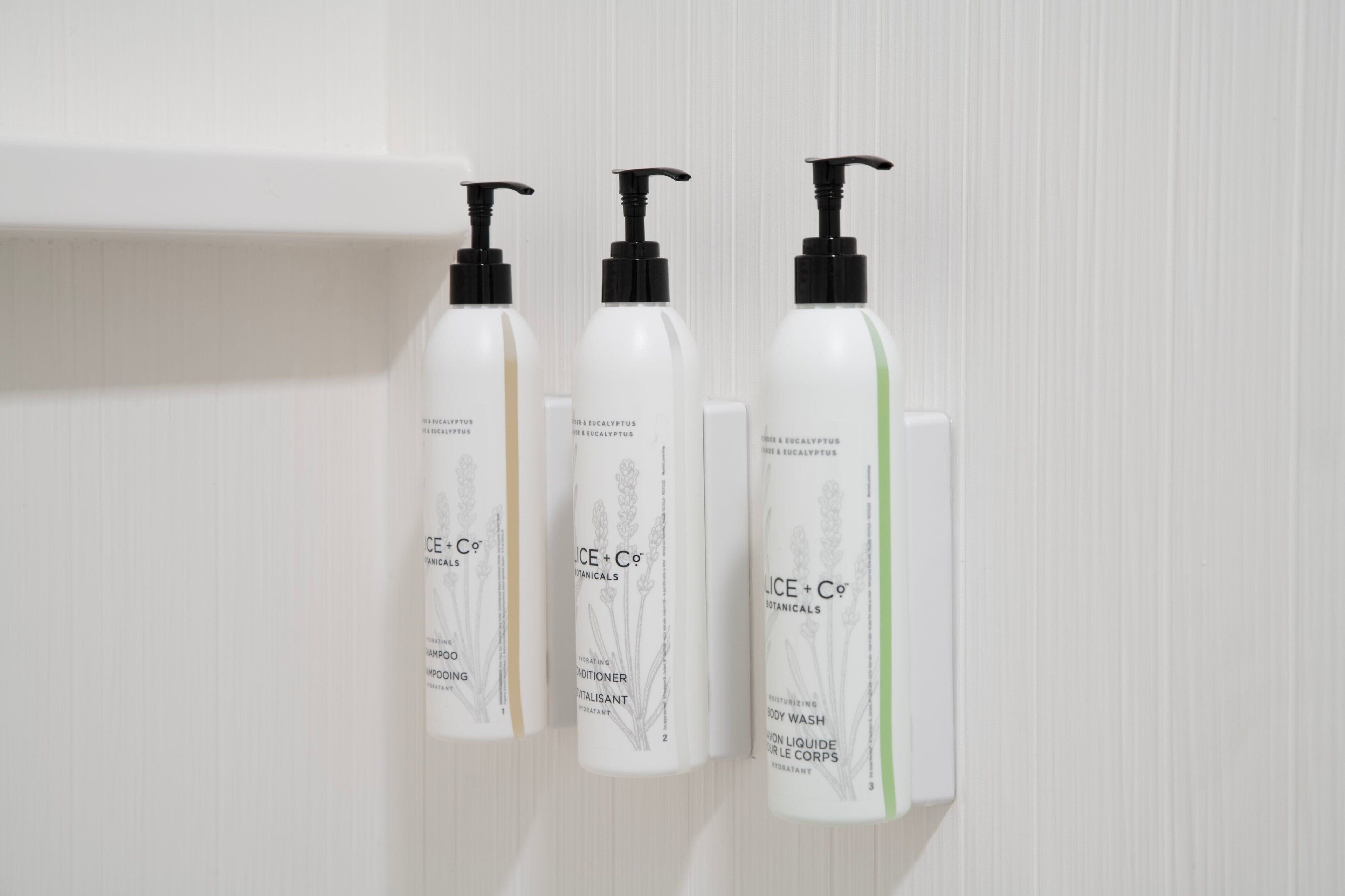 Three bottles of body wash and a soap dispenser on a white wall.