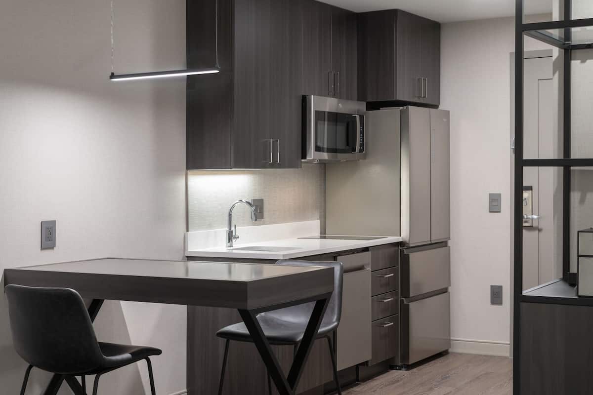 Une cuisine moderne avec des meubles de rangement de couleur sombre, un four à micro-ondes en acier inoxydable et un lave-vaisselle encastré.