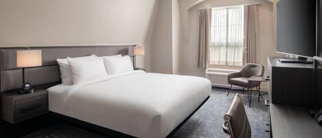 A hotel room with a large bed, a desk, a chair, a TV, and a window with curtains.