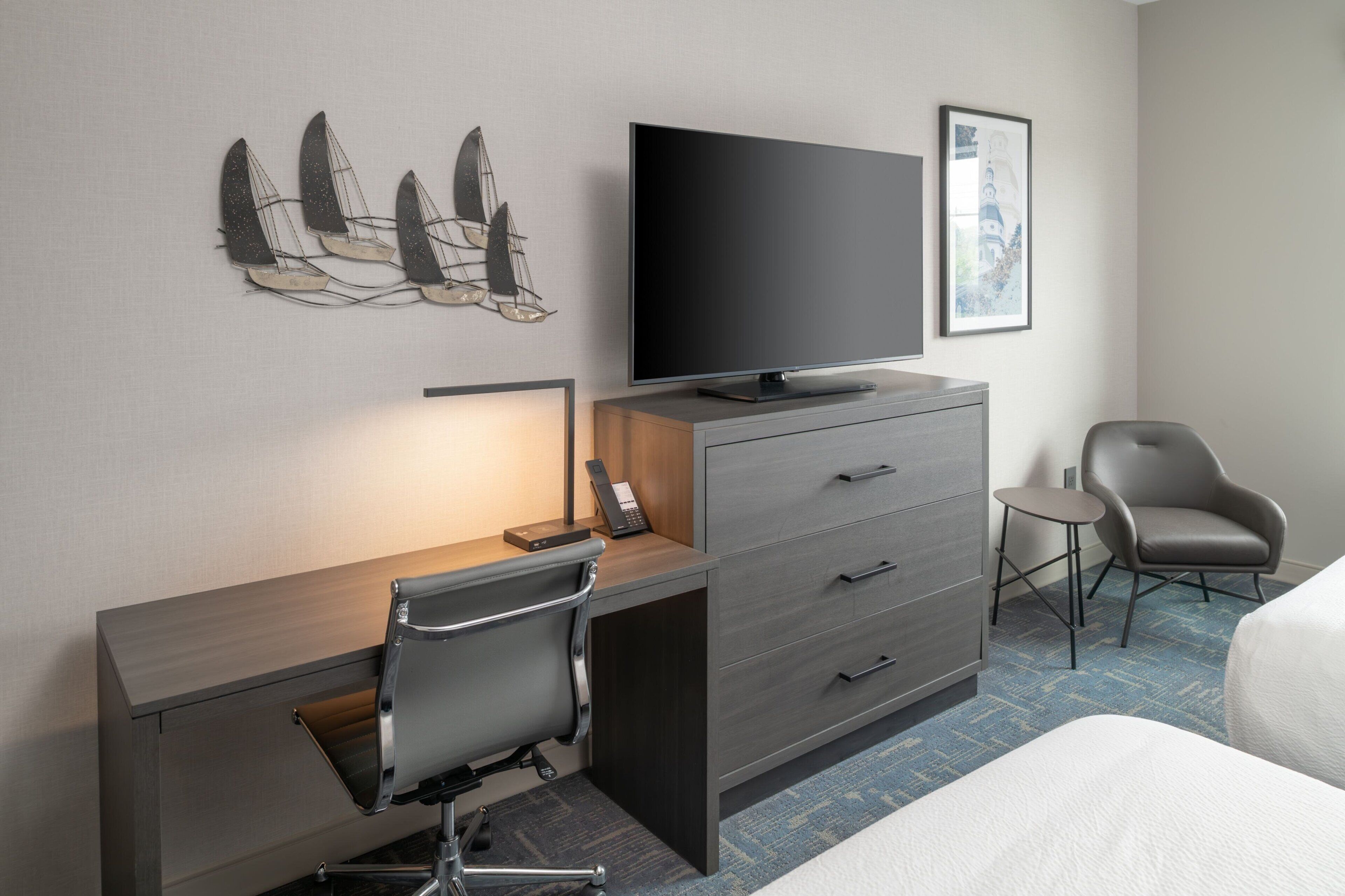 A hotel room with a desk, chair, television, and a small table.