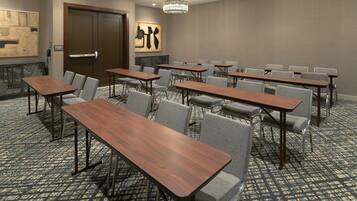 Un salón de conferencias con varias mesas y sillas, una puerta y una pared con arte abstracto.
