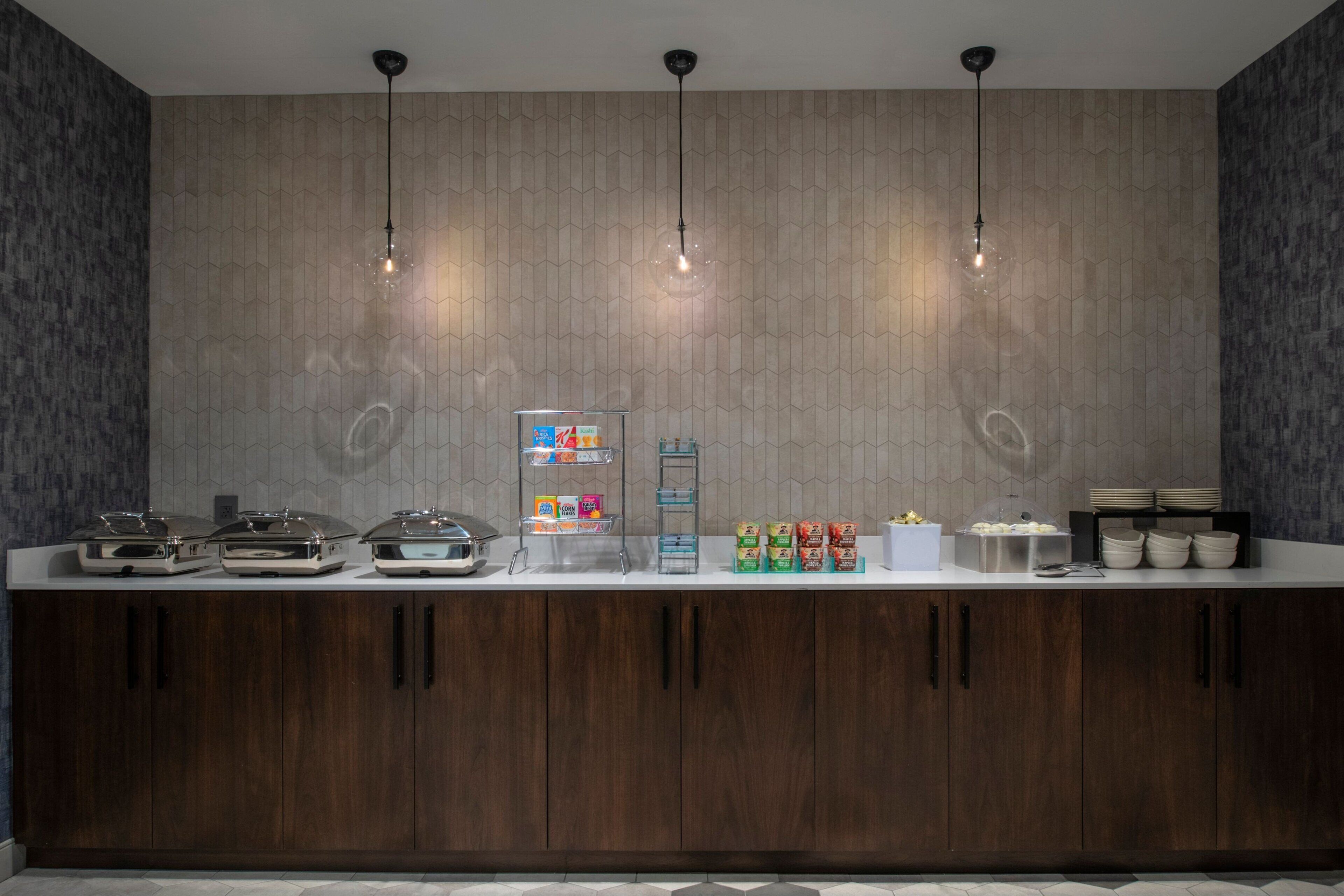 A modern kitchen with a wooden cabinet, a white countertop, and a hexagonal patterned backsplash. There are three pendant lights hanging above the counter.