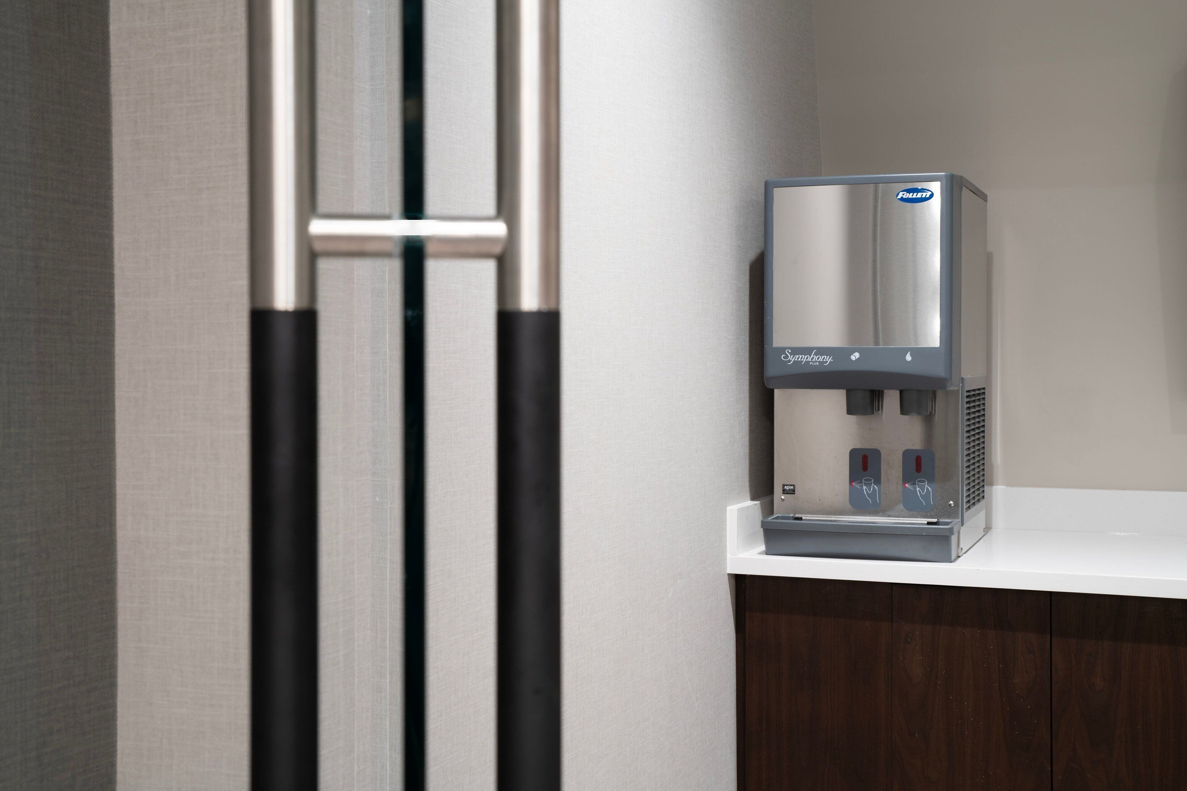 Un dispensador de agua sobre una encimera blanca, con diseño de acero inoxidable, un panel de control y un portabotellas.