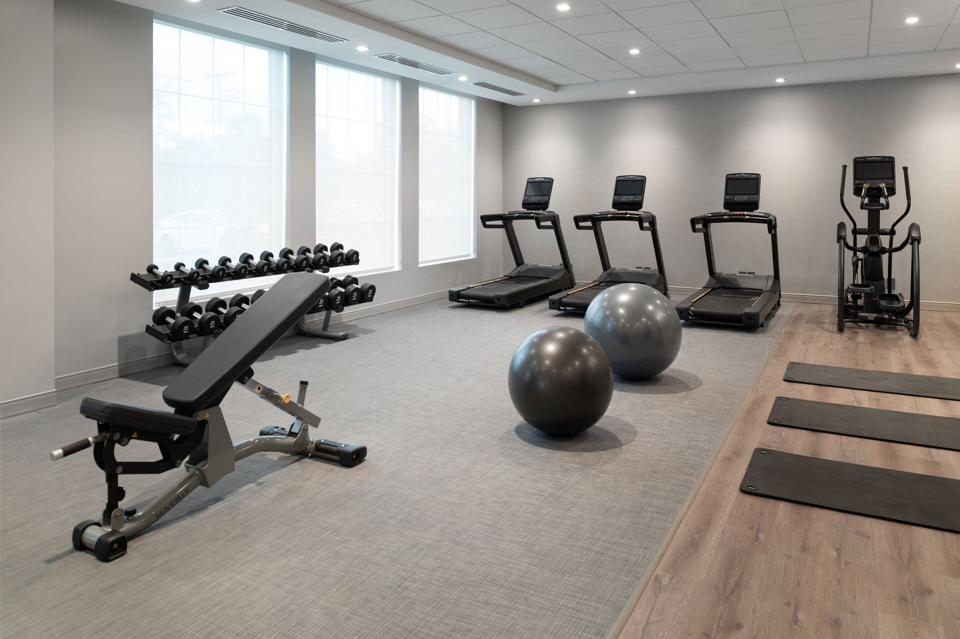 A gym with treadmills, dumbbells, a bench, and exercise balls.