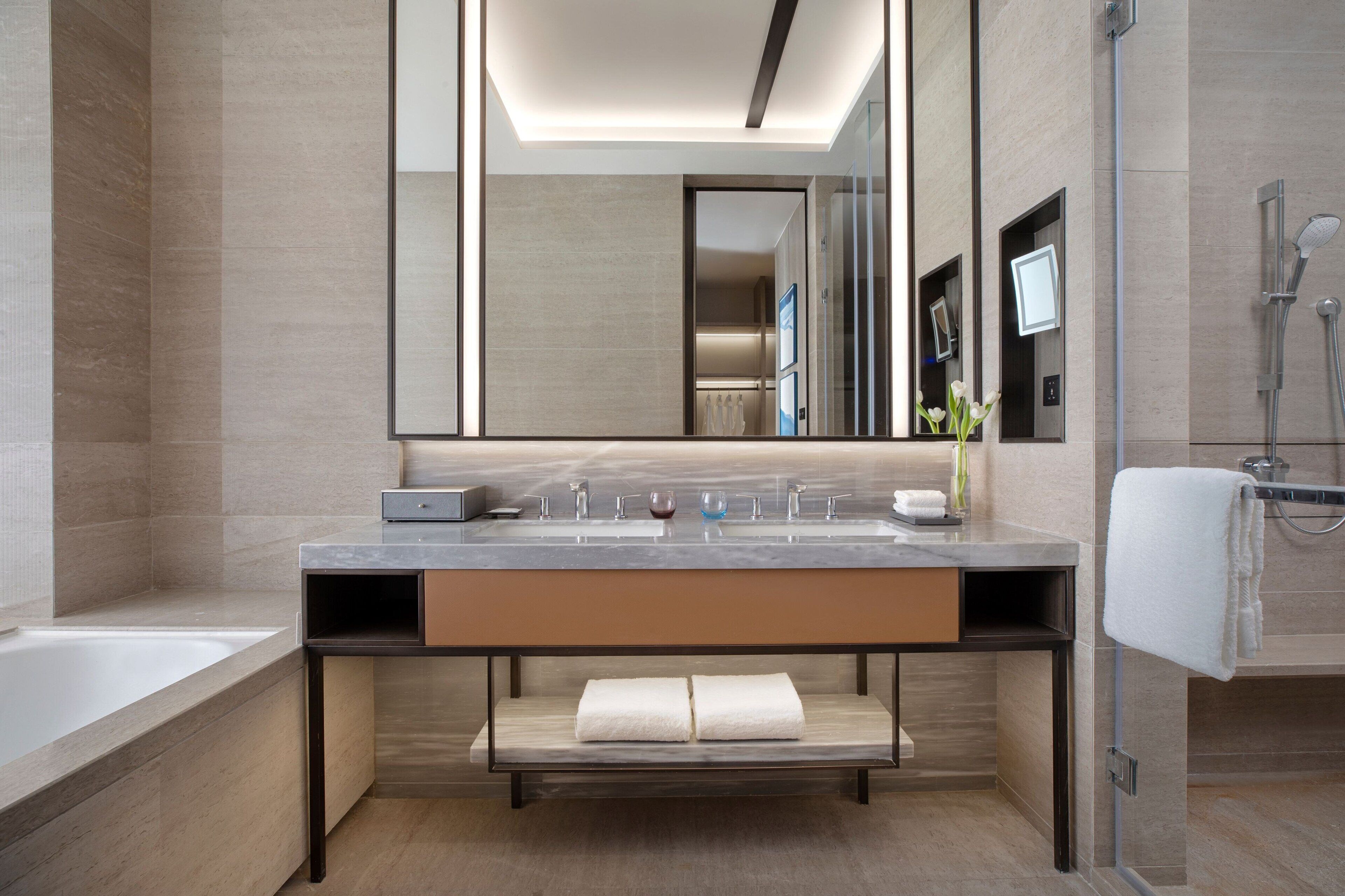 A modern bathroom with a large mirror, a bathtub, a shower, and a vanity with a sink and towel rack.