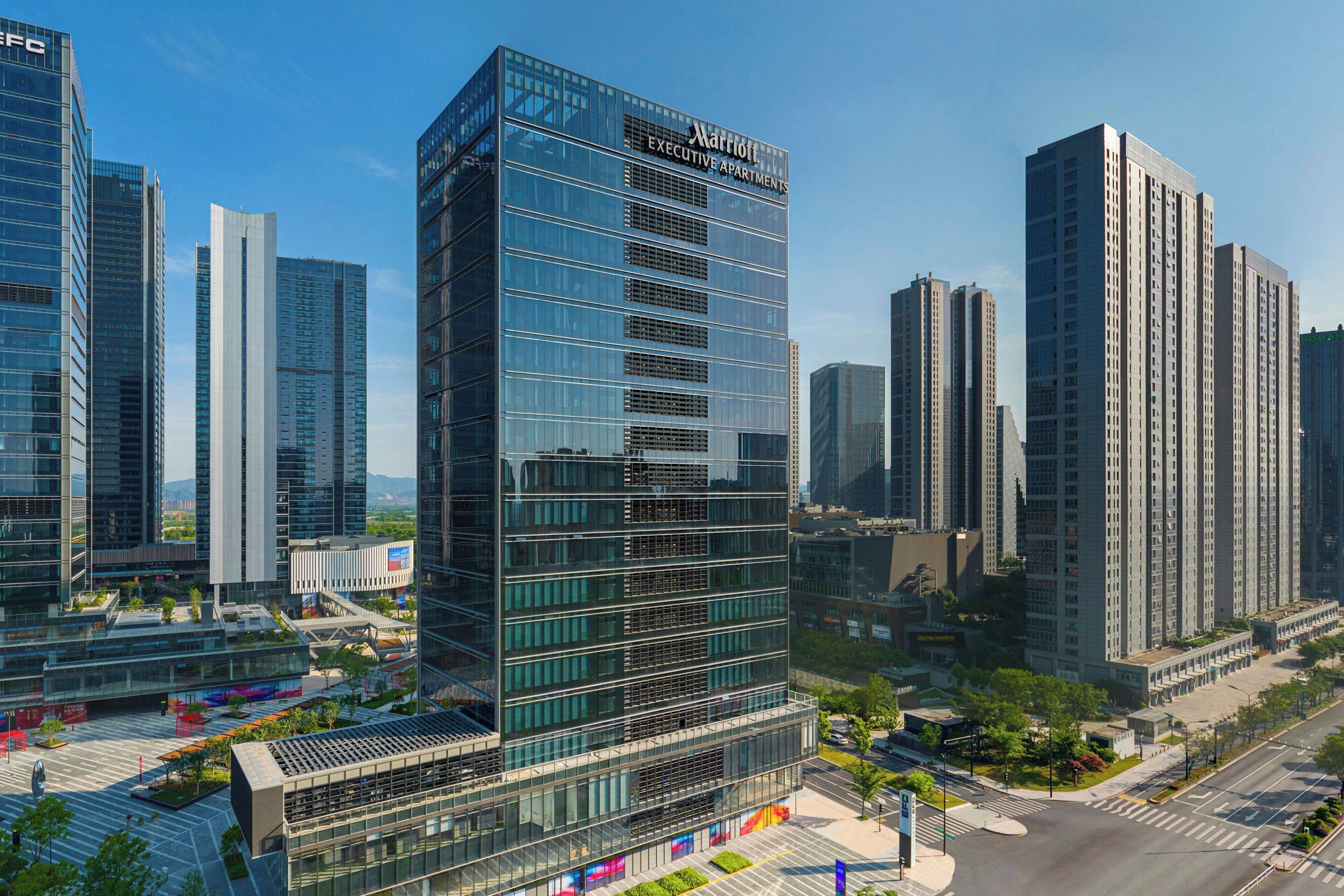 Um hotel moderno em formato de arranha-céu, com fachada de vidro, vários andares e um letreiro de destaque com a inscrição 'Marriott Executive Apartments'.