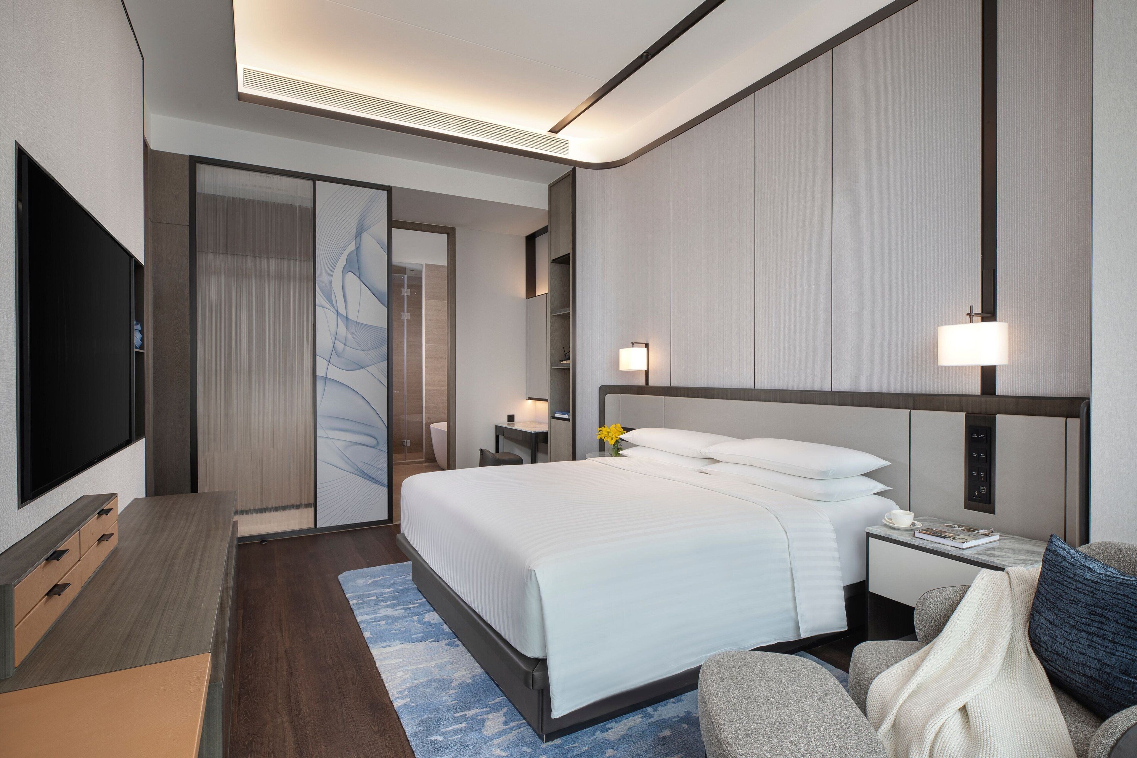 A modern hotel room with a large bed, a desk, a flat-screen TV, and a bathroom with a shower and toilet.