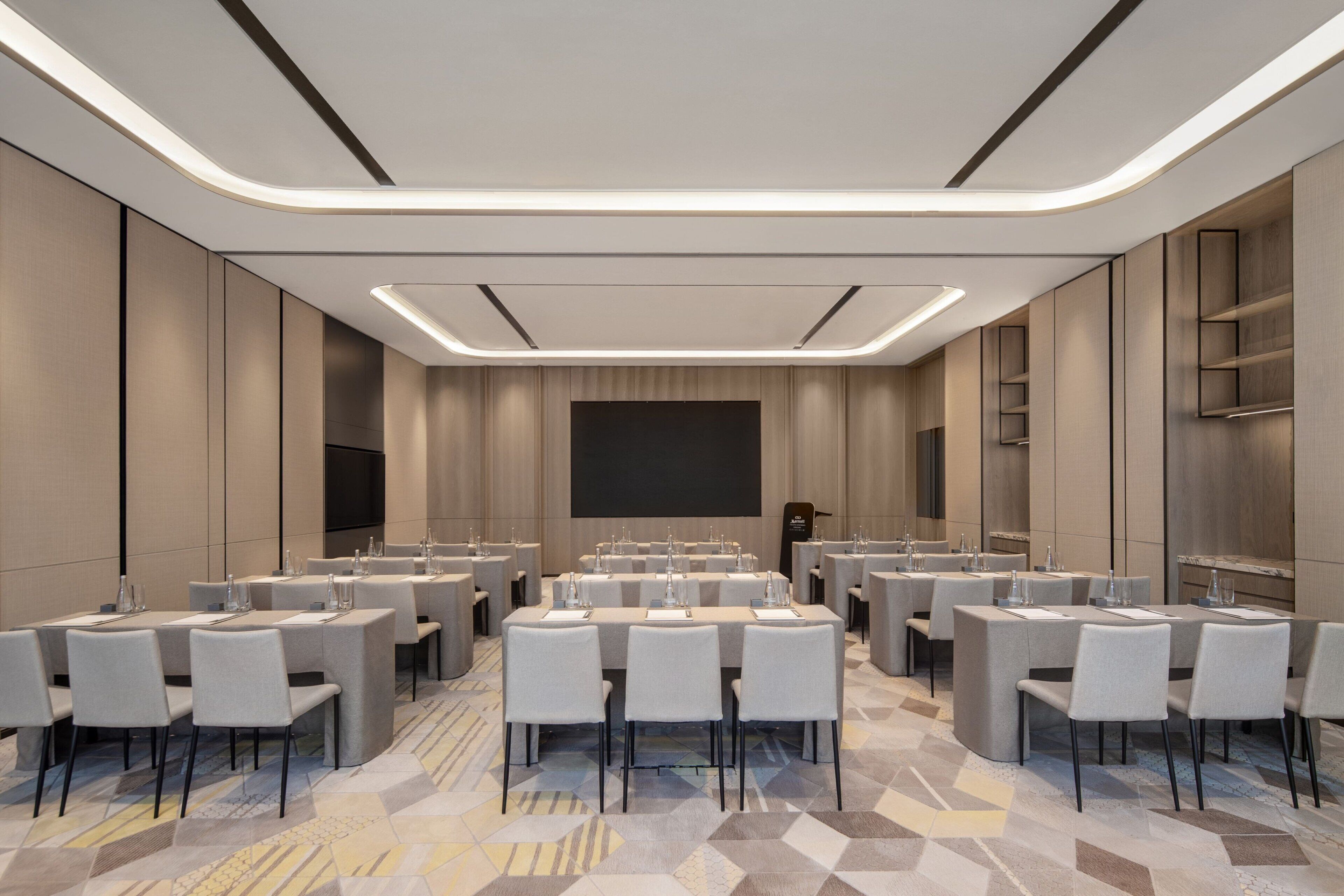 A conference room with multiple tables and chairs, a large screen, and a podium.