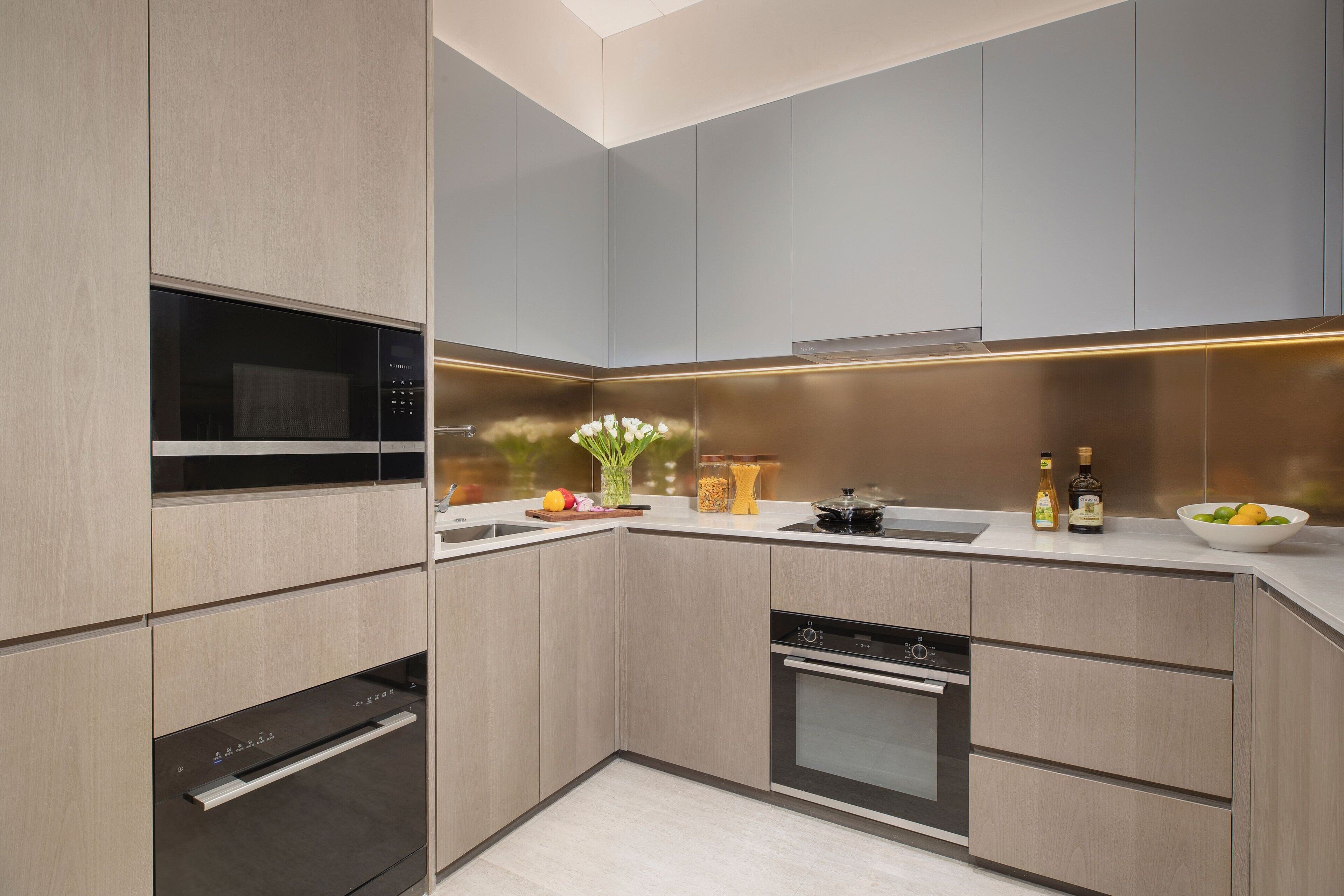 A modern kitchen with built-in appliances, a countertop with a bowl of fruit, and a vase of flowers.